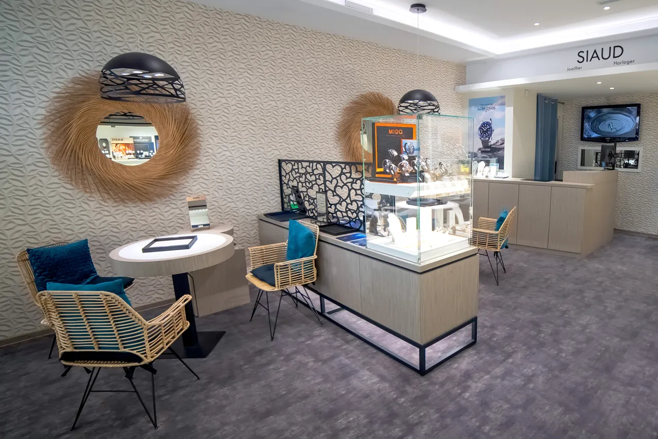Espace salon de la bijouterie SIAUD à Nice, fauteuils en rotin et vitrines sous l'enseigne joaillier horloger